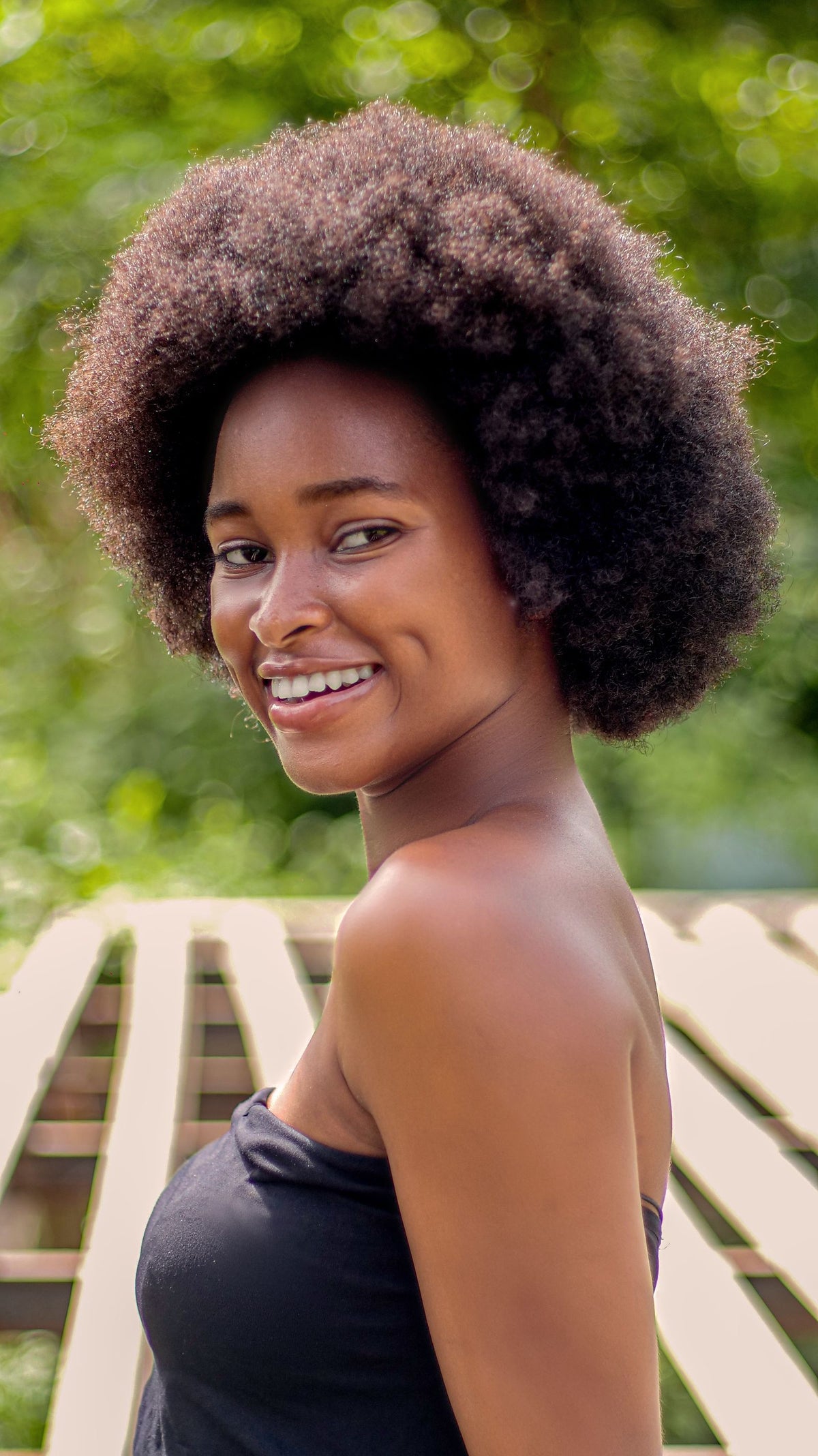 Mujer joven sonriente con rizos afro sanos y definidos, equilibrio de proteína e hidratación en cabello rizado