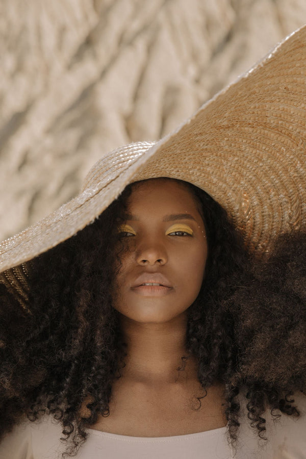 Mujer con cabello rizado definido usando sombrero para proteger sus rizos del sol